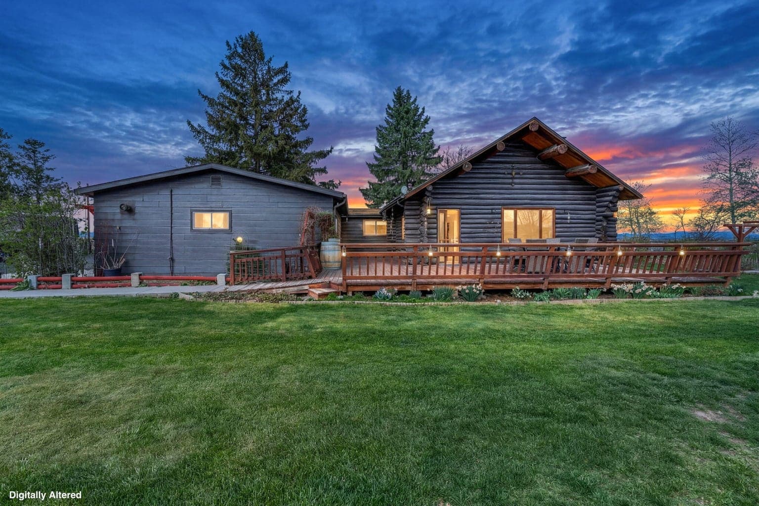 A sunset view of the back of the home showing the large wooden deck and manicured lawn.