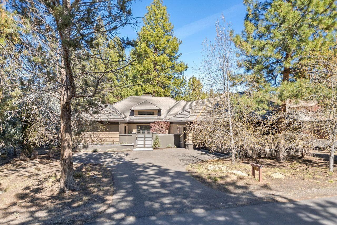 Front exterior showcasing the home’s understated architectural presence, set among mature Ponderosa pines within the gated Broken Top community. A gently curved driveway leads to a private, enclosed courtyard entry, creating a sense of arrival while maintaining privacy from the street. The warm, natural palette and clean rooflines reflect the home’s thoughtful design and seamless connection to its surroundings.
