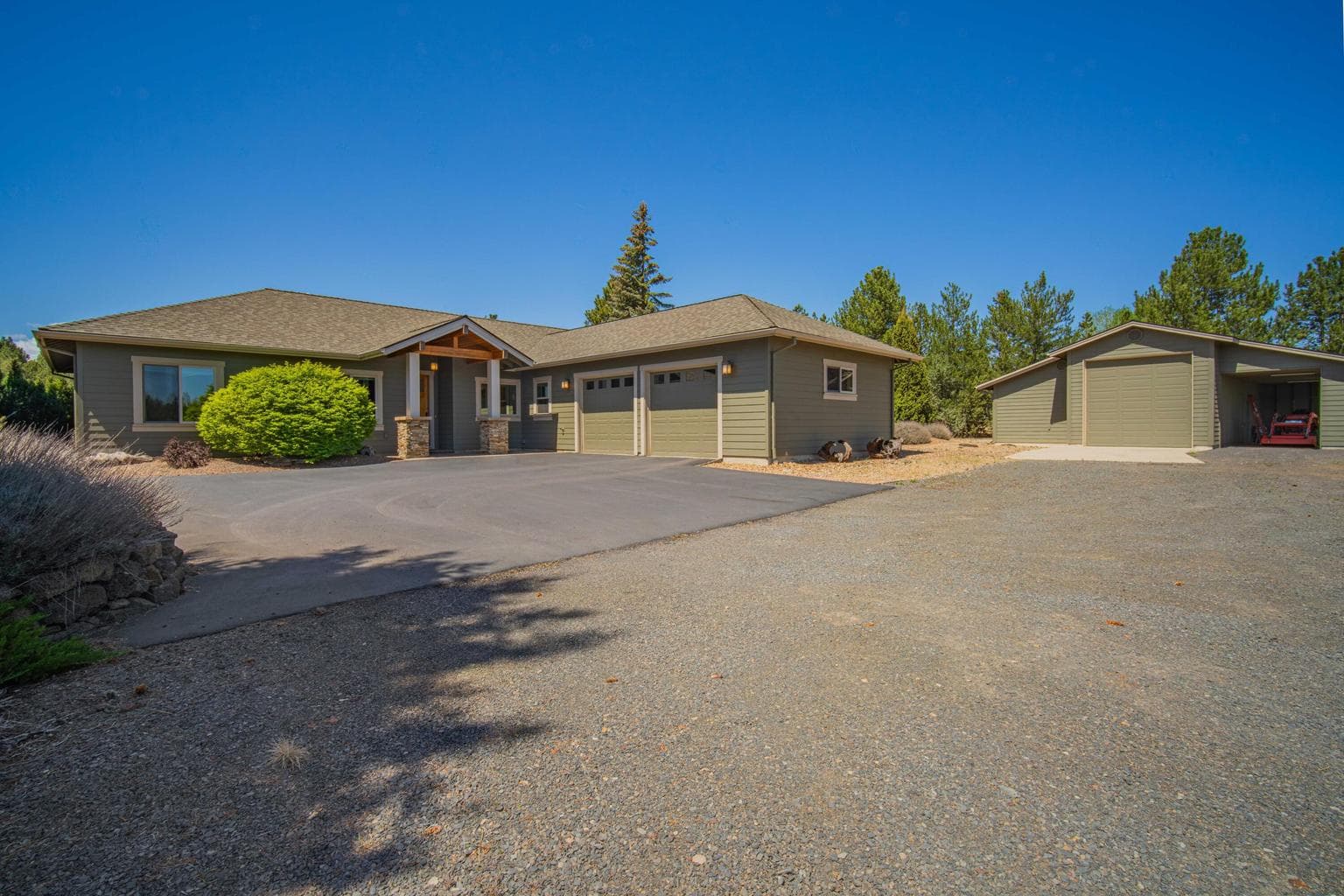 Front exterior view showing the home, detached barn/shop, generous parking, and natural low-maintenance landscape design.