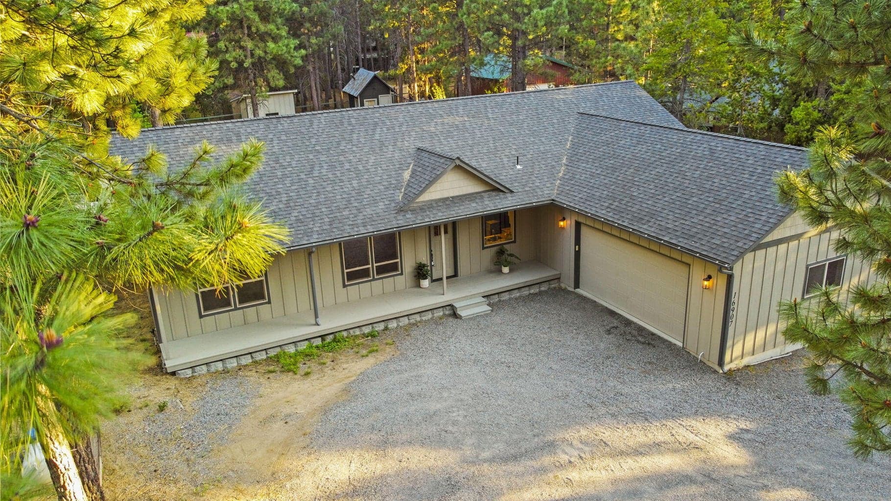 Aerial view of single-level modern farmhouse among mature pines.