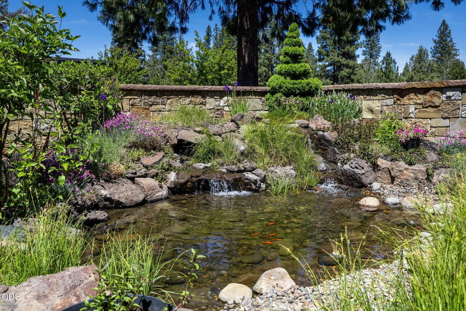 Beautifully landscaped courtyard with natural stone, flowering plantings, and a tranquil water feature that enhances the home’s sense of retreat.
